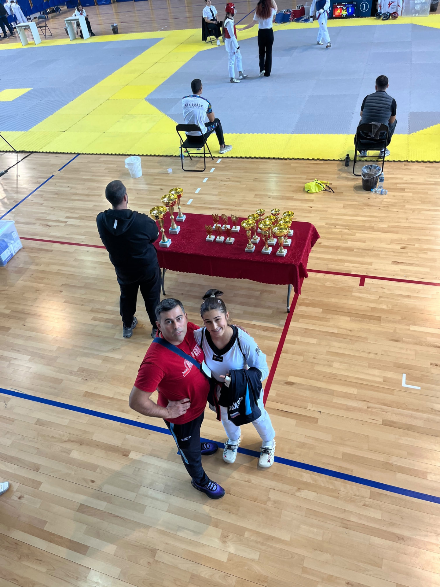 Coach and athlete standing together beside a table of trophies