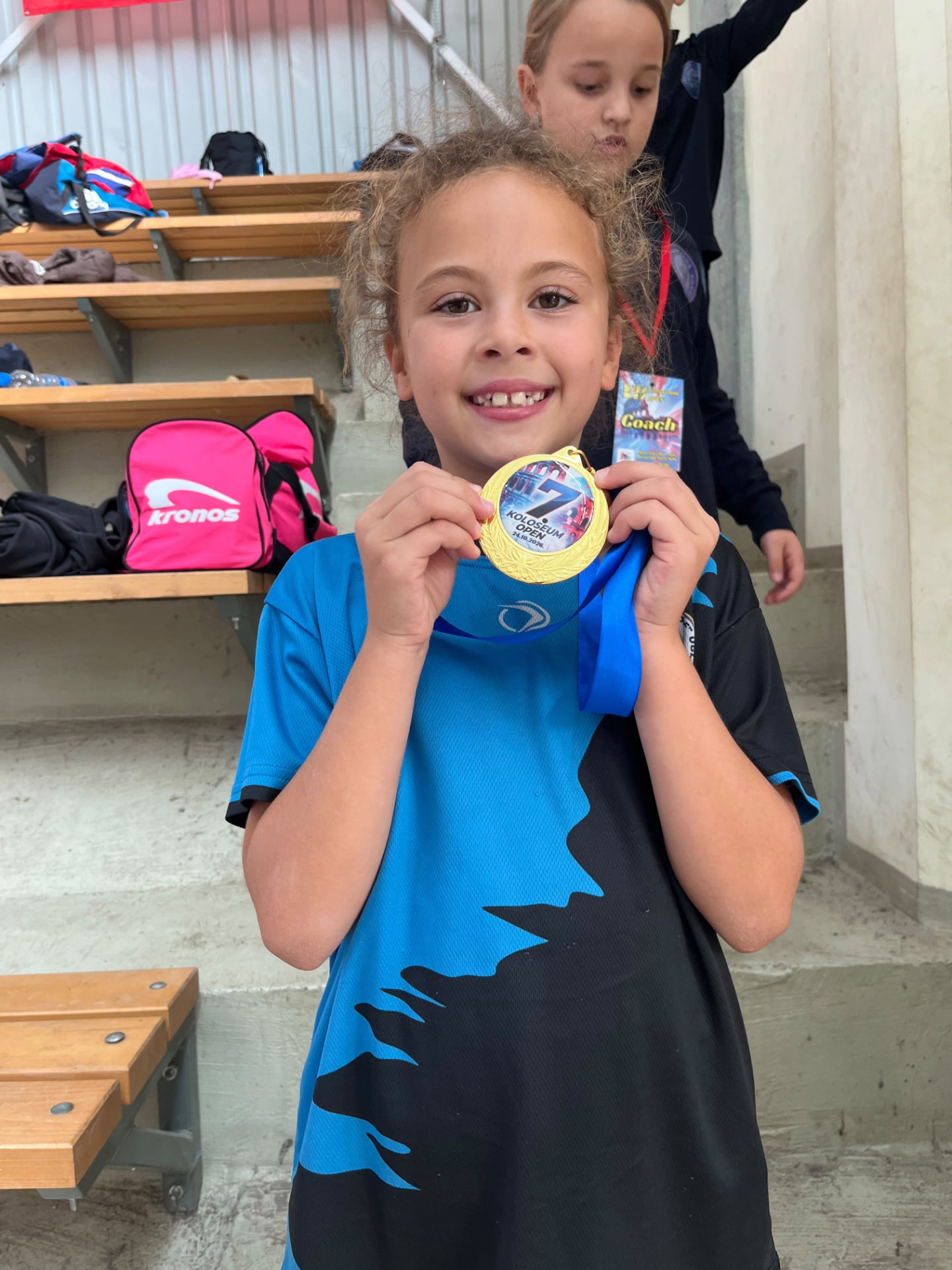 Young athlete smiling and holding up a gold medal from the Koloseum Open
